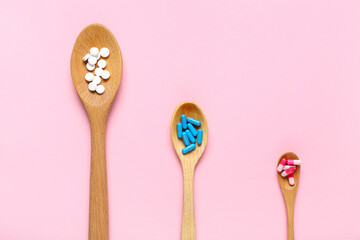 Wooden spoons with different pills on pink background