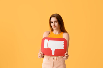 Displeased young woman holding dislike icon on orange background