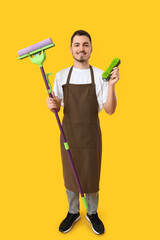 Male janitor with floor mop and brush on yellow background