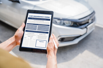 Man fills out a car insurance form after a car accident. Comprehensive motor insurance covers car damage. He files a claim report, speaking with an adjuster to understand his coverage and deductible.