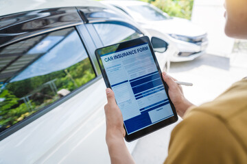 Man fills out a car insurance form after a car accident. Comprehensive motor insurance covers car damage. He files a claim report, speaking with an adjuster to understand his coverage and deductible.