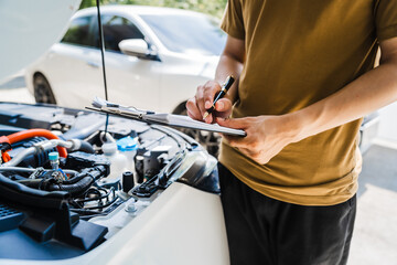 Man fills out a car insurance form after a car accident. Comprehensive motor insurance covers car damage. He files a claim report, speaking with an adjuster to understand his coverage and deductible.