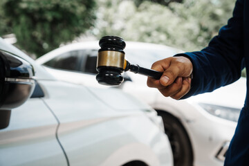 businessman in a suit and a lawyer, holding a wooden gavel, stand in front of a car, discussing...