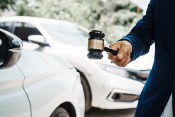 Fototapeta premium businessman in a suit and a lawyer, holding a wooden gavel, stand in front of a car, discussing legal aspects like citations, liability, and negligence related to a traffic violation...