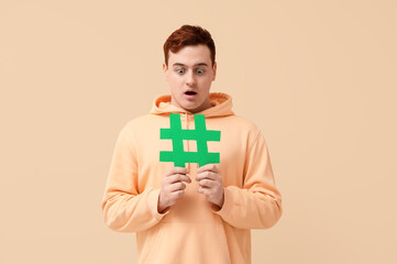 Shocked young man with hashtag sign on beige background