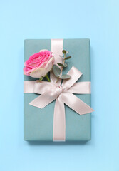 Gift box with beautiful rose and eucalyptus on blue background. International Women's Day