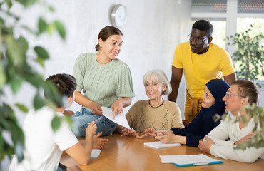 Group of multinational men and women discussing document while sitting at table in office..