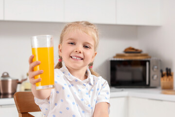 Cute little girl with glass of orange juice in kitchen