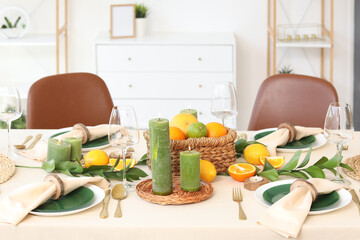 Beautiful table setting with citrus fruits and burning candles in living room