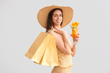 Beautiful young woman with shopping bags and glass of cocktail on grey background