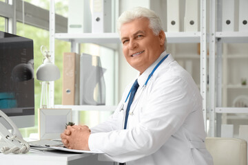 Mature doctor sitting at table in clinic