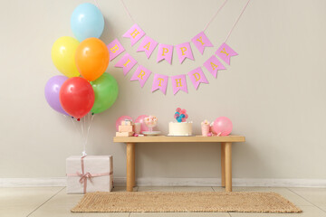 Table with cake, gift box and decor for birthday party against white wall