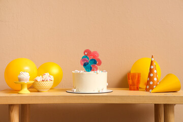 Table with cake, sweets and balloons for birthday party against beige wall