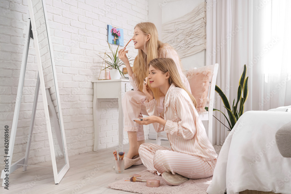 Sticker Beautiful young happy sisters in pajamas doing makeup at home