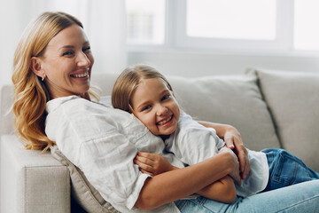 Mother and daughter share a cozy moment on the couch against a minimalist white background, smiling and bonding