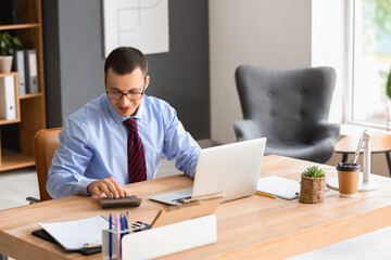 Male accountant working with calculator at table in office