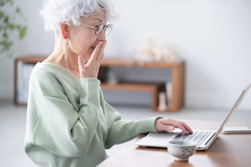 Surprised senior woman with her hand over her mouth while looking at a computer at a scam site or some phishing email A profile of a negative image
