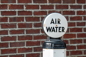Obraz premium A vintage red brick wall with grey mortar. There's an antique air and water pump for tires at a garage. The sign's lettering is black and the dome is made of white milk glass on a white and black post