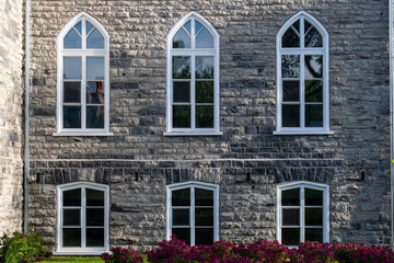 A historical concrete building, Gothic Revival style of architecture with multiple windows. Clean mason style with grey and beige bricks on the frame and six clerestory cathedral glass windows.