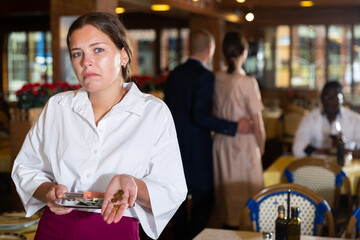 Discontented young waitress received small tips standing with money in restaurant