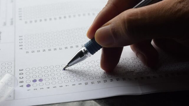 Hand of a person marking answers in OMR sheet. NEET, JEE, entrance test exam hall ticket student teacher coaching center pen paper career suicide multiple choice question s marks top rank study 