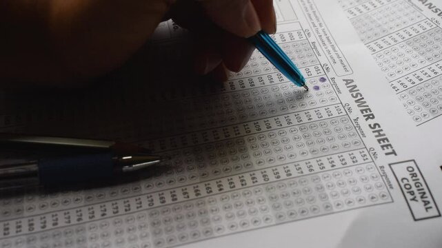 Hand of a person marking answers in OMR sheet. NEET, JEE, entrance test exam hall ticket student teacher coaching center pen paper career suicide multiple choice question s marks top rank study 
