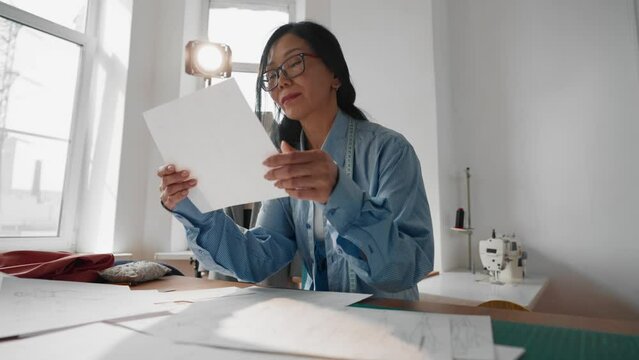 Seamstress woman viewing sketches and patterns in atelier, fashion business. Portrait of professional female designer of clothes working in her own studio, modern tailor-made atelier, creative hobby