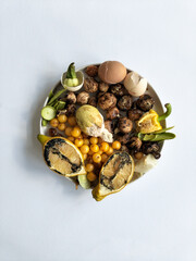 A plate with stacked products. Spoiled lemons, cherries, zucchini, mushrooms, pepper.  Remains of chicken shell