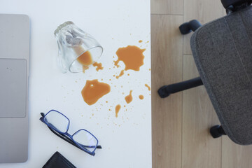 A drink was accidentally spilled on a desk with a laptop and glasses, creating a mess