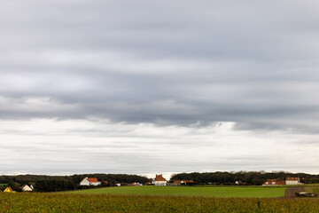 Obraz premium Peaceful rural landscape with cloudy sky and distant village, perfect for serene countryside themes.