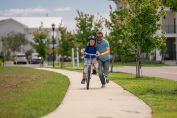 Fototapeta premium Little kid learning to ride bicycle with father on on summer holiday. Father teaching son cycling. Father and son learning to ride a bicycle at Fathers day. Father support and helping son. Child care.