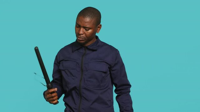 Security guard removing baton from belt, preparing to attack suspects. Portrait of bodyguard pointing finger towards truncheon, threatening to subdue criminals, studio background, camera A