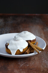 Side View of Cinnamon Buns with White Icing and Cinnamon Sticks on Baking Sheet
