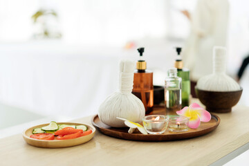 Beauty treatment items for spa procedures such as essential oils, Thai herbal compress, flowers, sliced cucumber and tomato on the table with a blur customer in the background. Image with copy space
