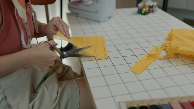 designer is cutting fabric according to the pattern the customer wants, a tailor cuts large pieces of cloth that has been measured to the desired size in oder to make a garment