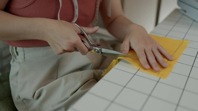 designer is cutting fabric according to the pattern the customer wants, a tailor cuts large pieces of cloth that has been measured to the desired size in oder to make a garment
