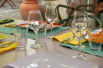 Beautifully set table in the garden. Colorful plates and glasses on placemats. Cutlery on yellow napkins. Mediterranean ambience