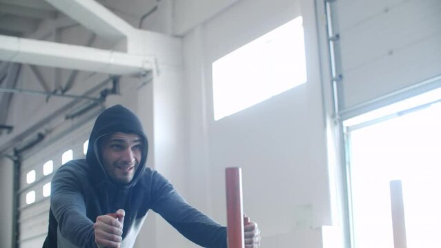 Determined male athlete taking break after pushing heavy sled. Sportsman wearing hooded iacket exercising at gym. He is getting tired while doing strength training on sunny day. 
