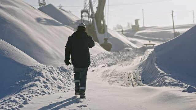 Worker walks on construction site on winter day. Stock footage. Worker at snow-covered quarry on winter day. Snow covered heavy machinery at quarry in winter