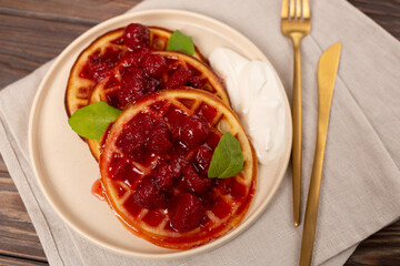 A portion of Viennese waffles on a plate with strawberry jam and sour cream
