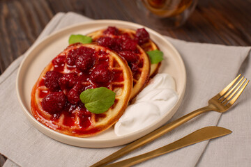 A portion of Viennese waffles on a plate with strawberry jam and sour cream