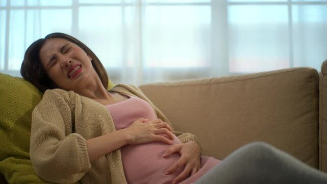 Young pregnant woman suffering from abdominal pain alone at home, female feel abnormal painful contraction during pregnancy, accidental medical urgency case and health care insurance for pregnancy.
