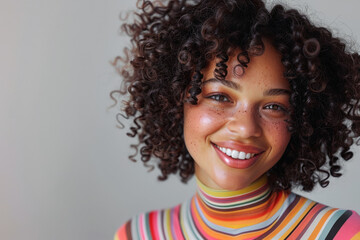 A smiling African American woman with vibrant curly hair, wearing a colorful striped top
