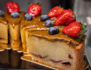 Pistachio cake decorated with strawberries and blueberries on shelf in bakery shop.