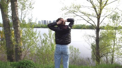 A woman enjoys the view of the landscape while standing by the river. View from the back.