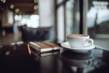Comfortable workplace on table by the window in modern cafe with coffee drink and  note book, vintage tone