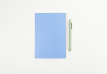 Top view of blue notebook, green pen on white background. School, office wallpaper. Flat lay, copy space.