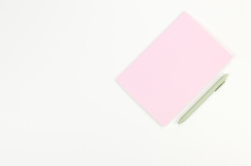 Top view of pink notebook, green pen on white background. School, office wallpaper. Flat lay, copy space.