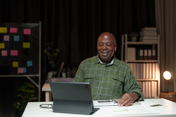 Happy African American man looking at laptop computer screen, typing, searching for information, checking email, chatting on social network. Freelance blogger working on online projects.