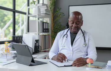 African American male doctor working in clinic at desk using laptop in medical coat and stethoscope. organ specialist The patient's anatomy, treatment methods, medical treatments.